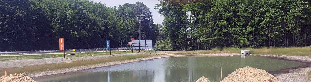A large green and brown covered pool of water located at the front of the community.  